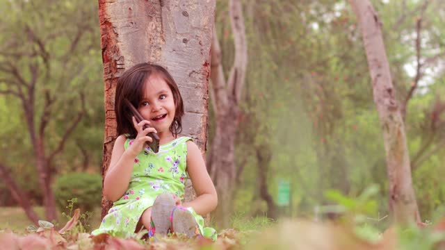 Baby girl talking on mobile phone outdoors in the park