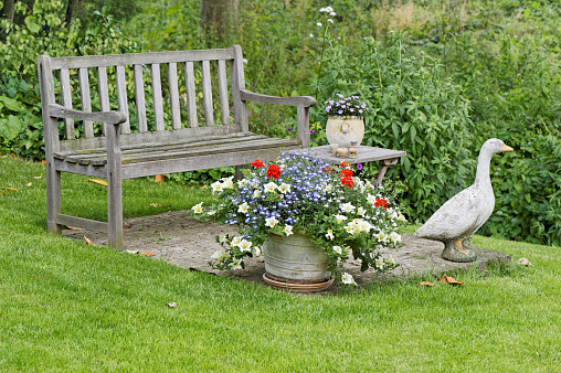 Garden with wooden bench,stone ornament, side table  and flower pots in summer.