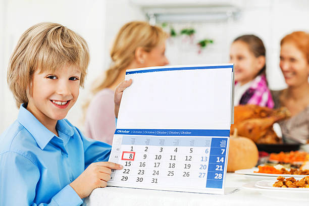 Family at the Thanksgiving dinner. Cute boy is holding a calendar and pointing at the date. Focus on the boy.