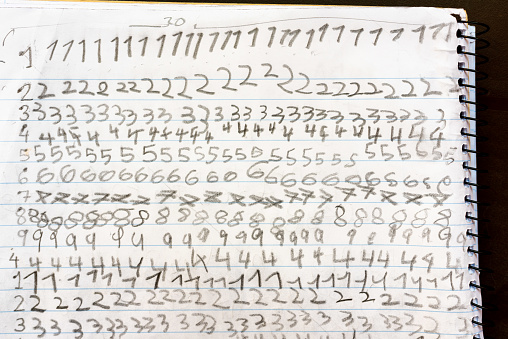 Numbers written by a child repeated on the sheet of paper notebook at school.