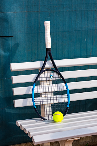 Tennis racket standing on a bench with a tennis ball