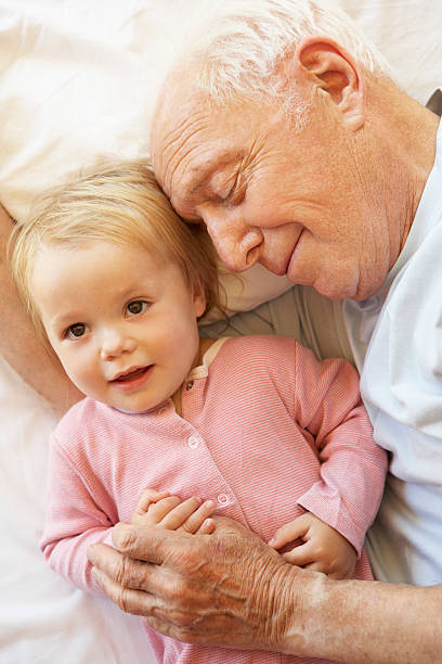 Grandfather Cuddling Granddaughter In Bed Grandfather Cuddling Granddaughter In Bed Smiling. sleeping grandpa stock pictures, royalty-free photos & images