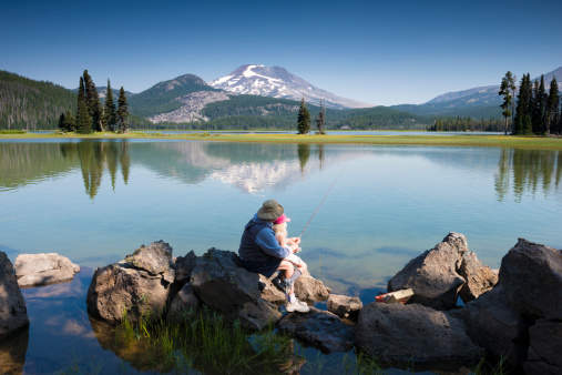 A fisherman teaching his five year old granddaughter how to fish. Located at the stunningly beautiful Sparks lake, Central Oregon, USA on typical sunny morning.