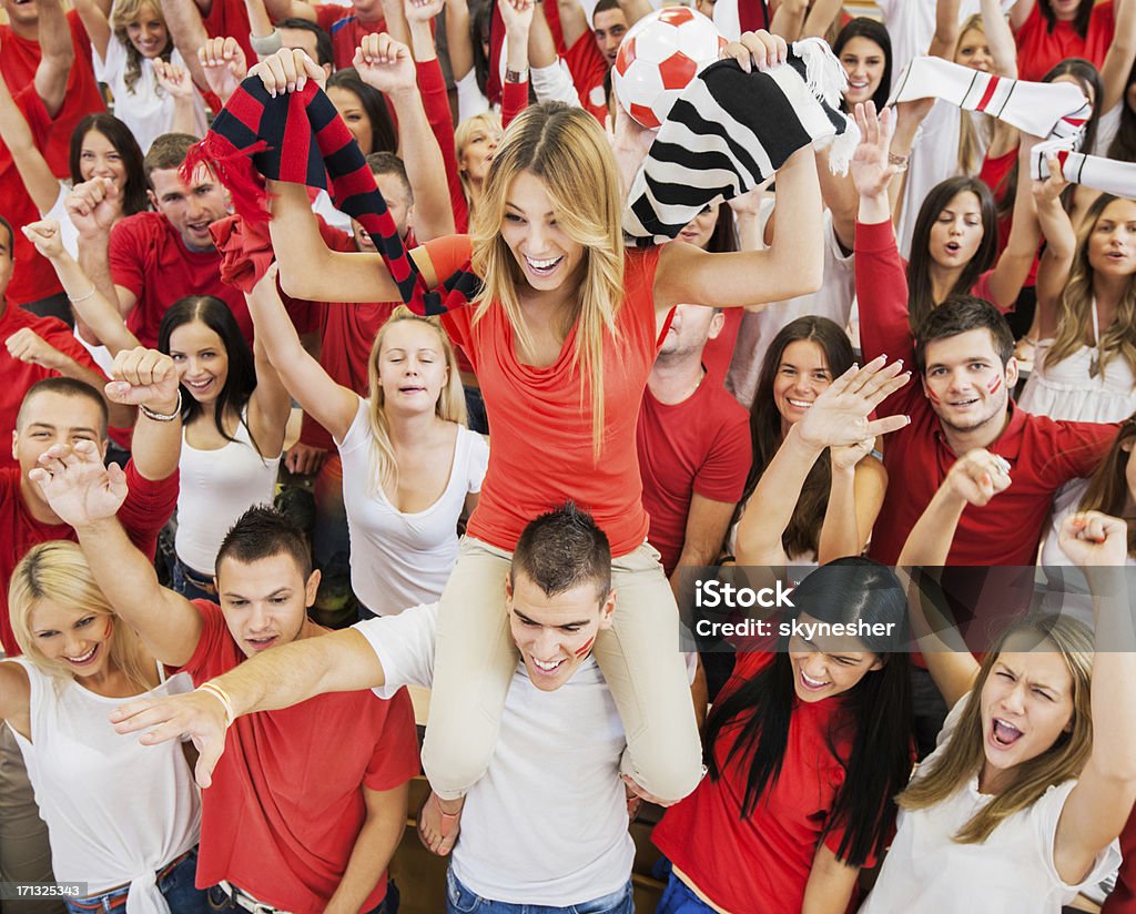 Group of football fans cheering. Large group of ecstatic football fans cheering. They are wearing white and red t-shirts.  Adolescence Stock Photo