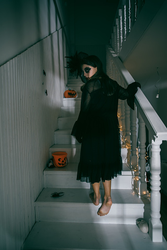 Spooky scenary of a Teenage girl dressed in a witch costume  climbing the stairs ready for the Halloween party