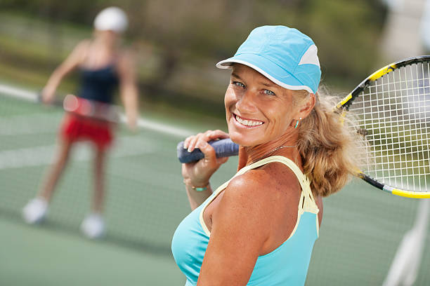 Mature woman tennis portrait Close-up of mature woman tennis player ready to play looking at camera. opponent in background. tennis senior adult adult mature adult stock pictures, royalty-free photos & images