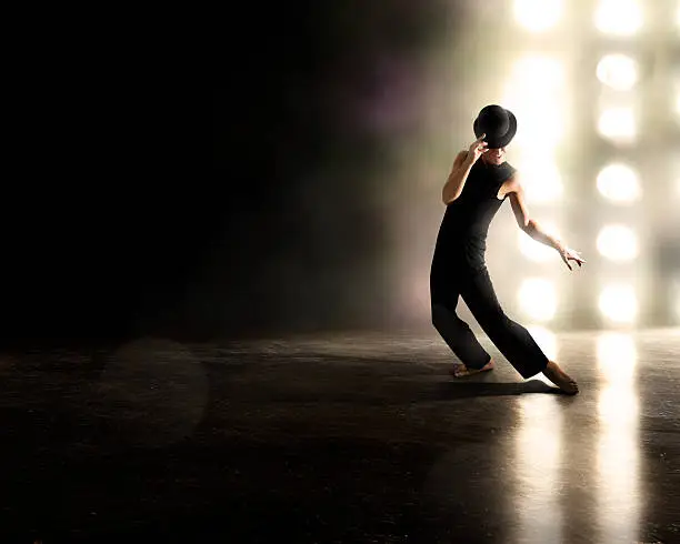 Male dances against backlighting with derby hat.