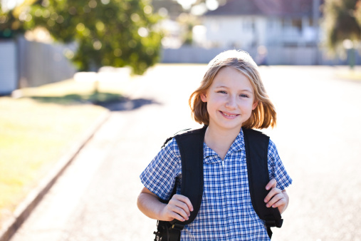 Happy smiling school girl walking home from school with her backpack on - wearing school uniform outdoors with shallow depth of field - high key effect. Click to see more...