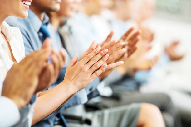 Group of businesspeople sitting in a line and applauding. Group of cheerful businesspeople sitting in a row on a presentation and clapping. press conference photos stock pictures, royalty-free photos & images