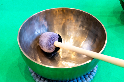 Singing bowl with clapper on a blue ball base and a green carpet table shining under light
