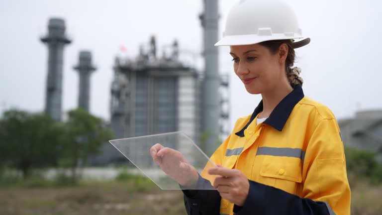 Caucasian engineer making a significant impact at a power plant. Confidently beside a power plant generator to reduce factory waste to zero. Analyzes data on the transparent glass tablet utilizing graphic interface dashboard with high technology.