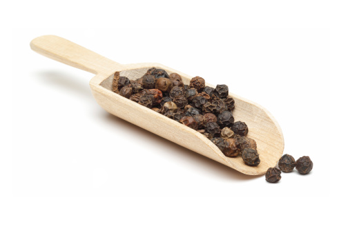 Black peppercorns on a wooden spoon - cutout