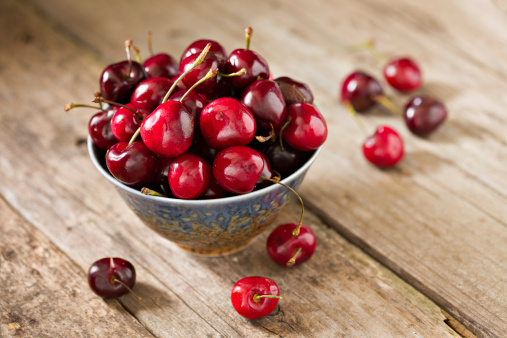 A high angle view of a blue ceramic bowl full of recently picked cherries. Shot on an old wooden  background.