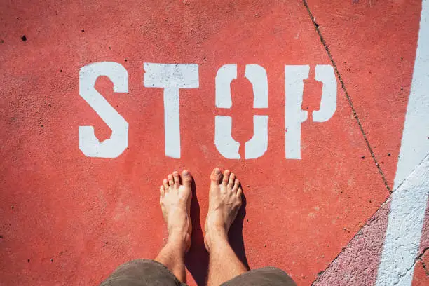 A man in bare feet stops at a stop mark painted on the ground.