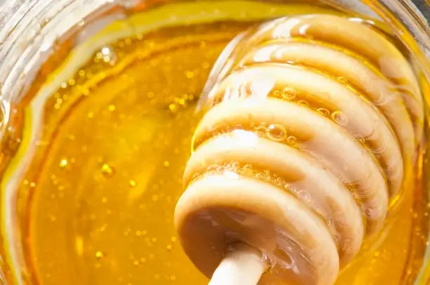Wooden Honey drizzler dipping into a pot of Pure golden manuka honey