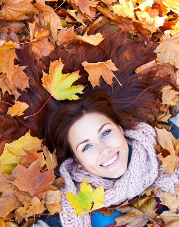 Woman with red hair laying on autumn leaves. She has gloves and a multicolored sweater.