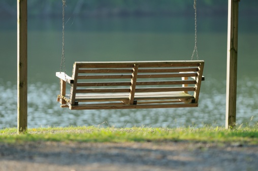 Wooden porch swing by river at sunrise or sunset.