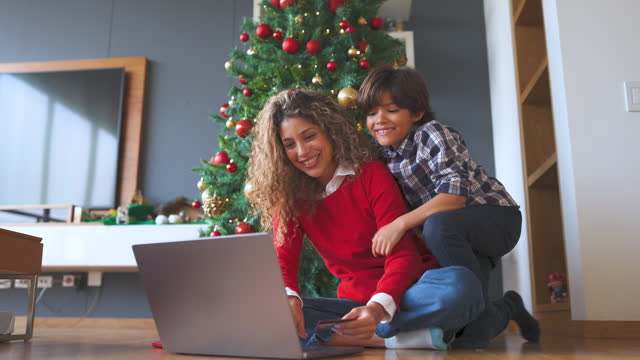 Loving son hugging mother from behind while she is Christmas shopping online using a laptop and credit card both looking very happy