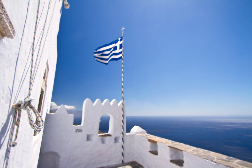 Greek flag waving in the sky at the famous monastery of Monastery of Hozoviotissa in Amorgos.