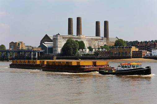 View of a barge carrying containers on Thames with the Greenwich Power Station in the background.