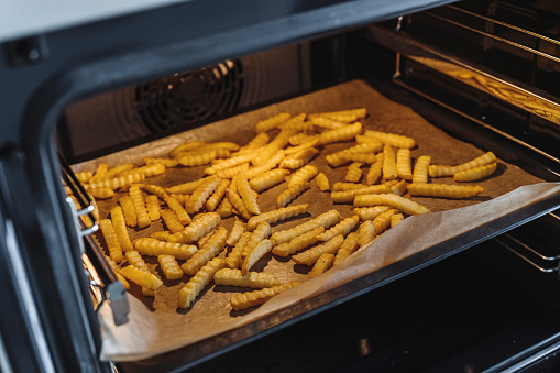Crispy French fries spread out on an oven tray, lined with baking paper.