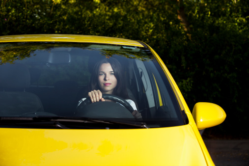 woman behind the wheel of a yellow car seen trough the windshield
