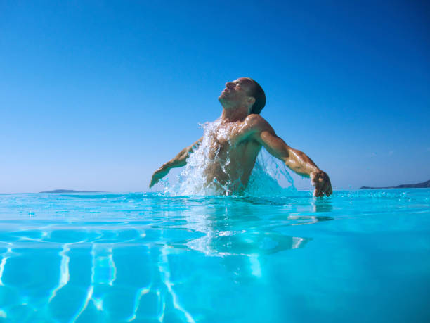 Athletic Man Emerges From Rippling Blue Water Athletic man emerges with a splash from rippling blue water caucasian appearance stock pictures, royalty-free photos & images