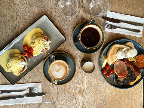 Breakfast for two on a wooden table in a cafe. Full English breakfast and eggs royal. Charming rustic style ceramic plates and coffee cups.
