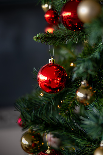 Three of four candles are burning for the third Advent on fir branches with Christmas decoration against a grey background, copy space, selected focus, narrow depth of field