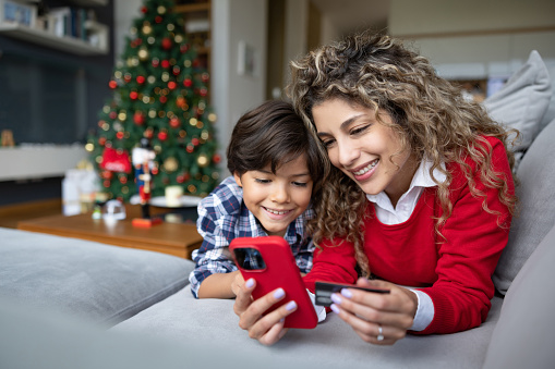 Happy mother and son shopping their Christmas presents online using her cell phone and paying by credit card - e-commerce concepts