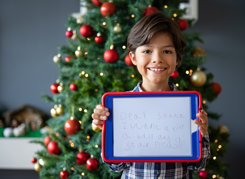 Portrait of a happy Latin American boy writing a letter for Santa using a tablet and looking at the camera smiling