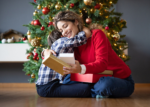 Happy mother hugging her son after getting a Christmas present from him and smiling - holiday season concepts