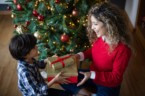 Loving son giving a Christmas present to his mother at home - holidays season concepts
