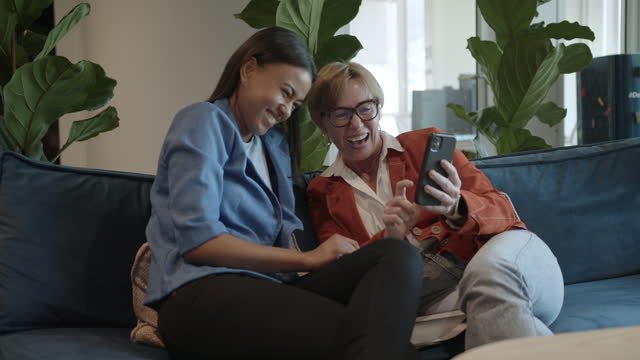 Diverse businesswomen laughing at smart phone photos during an office break