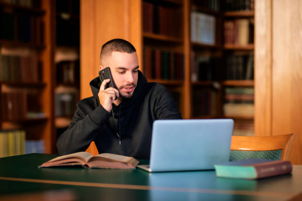 istock Male student sitting in the university library and using notebook and mobile phone 1713348310