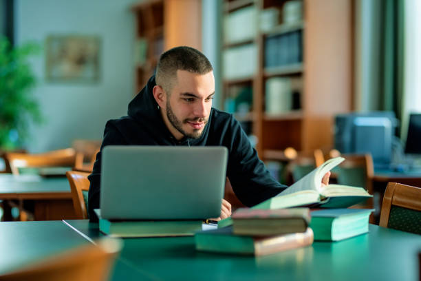 istock Male student using notebook and books and learning in the university library 1713348312