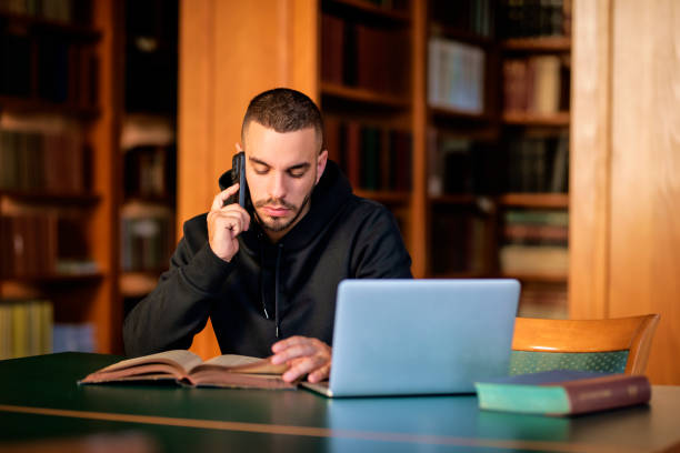 istock Male student sitting in the university library and using notebook and mobile phone 1713348338