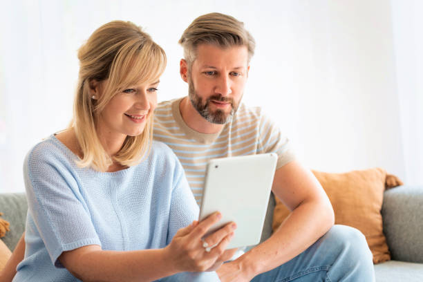istock Blond haired woman and handsome man sitting on the sofa at home and using digital tablet 1713348350