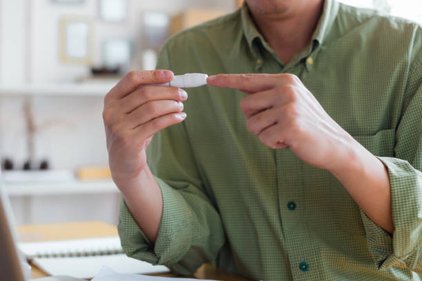 primo piano delle mani dell'uomo usando la lancetta sul dito a casa per controllare il livello di zucchero nel sangue. mani tagliate di glaucometro durante l'esame del test della glicemia a casa. - glaucometer analyzing blood equipment foto e immagini stock