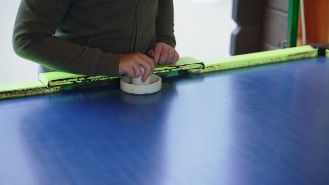 Boy hits air hockey puck with plastic bat on old shabby table.