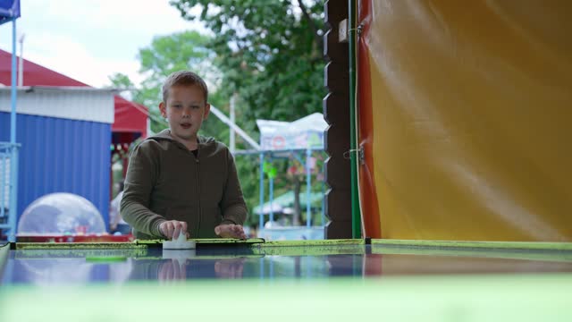 Boy is emotionally, actively playing air hockey in amusement park.