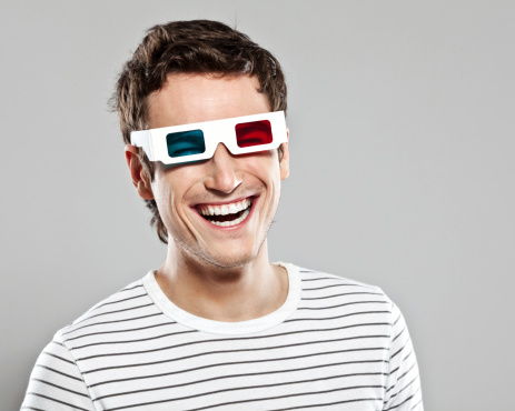 Portrait of happy young man wearing 3D glasses. Studio shot, grey background.