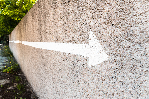 Arrow with a white line painted on a stone wall with negative space and copy space to indicate direction.