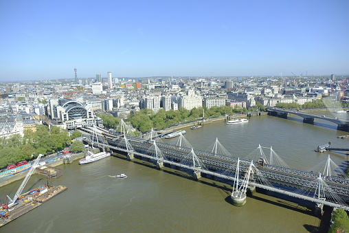 Wide angle view of boat traffic on water, moored warship, and landmark 19th-century bridge crossing near Tower of London on sunny summer day.