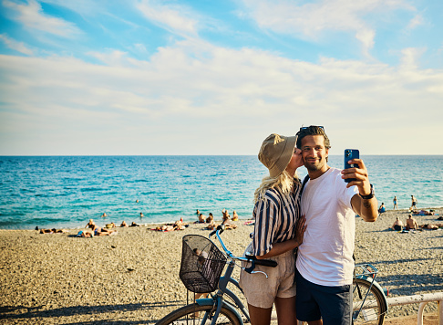 Happy young adult couple taking a selfie on the Promenade des Anglais in Nice, France.