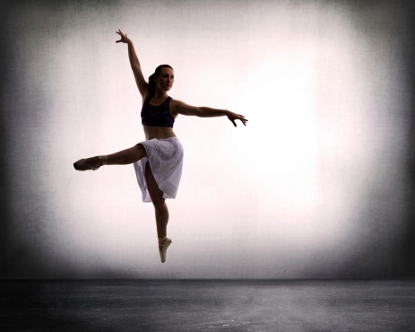 Female dances in ballet pointe shoes against a backlit wall.