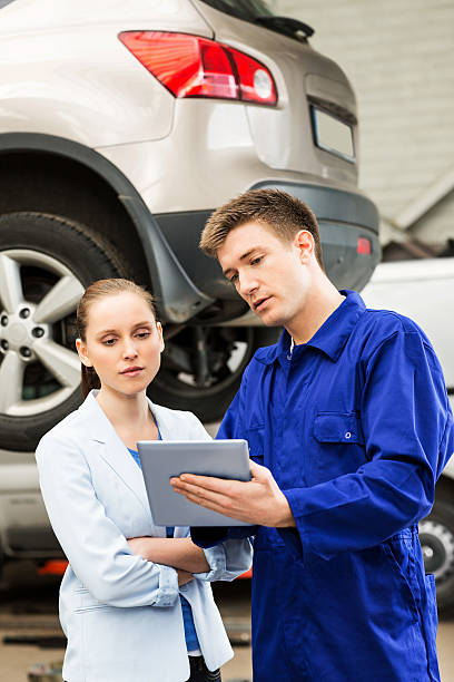 Mechanic With Customer Using Digital Tablet Mechanic with young female customer using digital tablet in garage. Vertical shot. auto repair shop mechanic digital tablet customer stock pictures, royalty-free photos & images