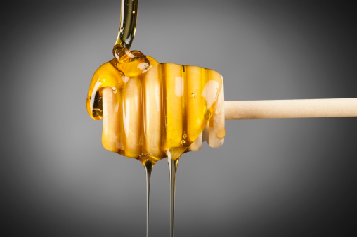 Pure golden honey pouring over a wooden serving drizzler