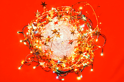 Round Christmas composition made of tinsel Christmas bauble and electric lights on red background