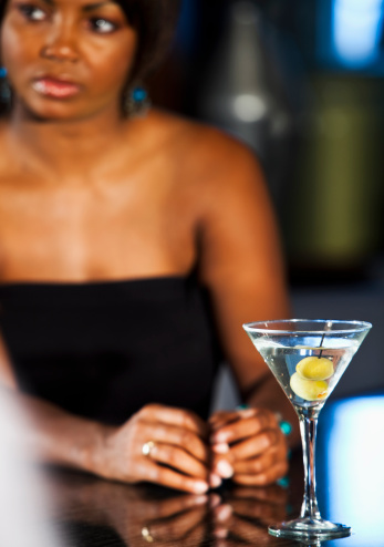 African American woman at bar with martini.  Focus on glass.